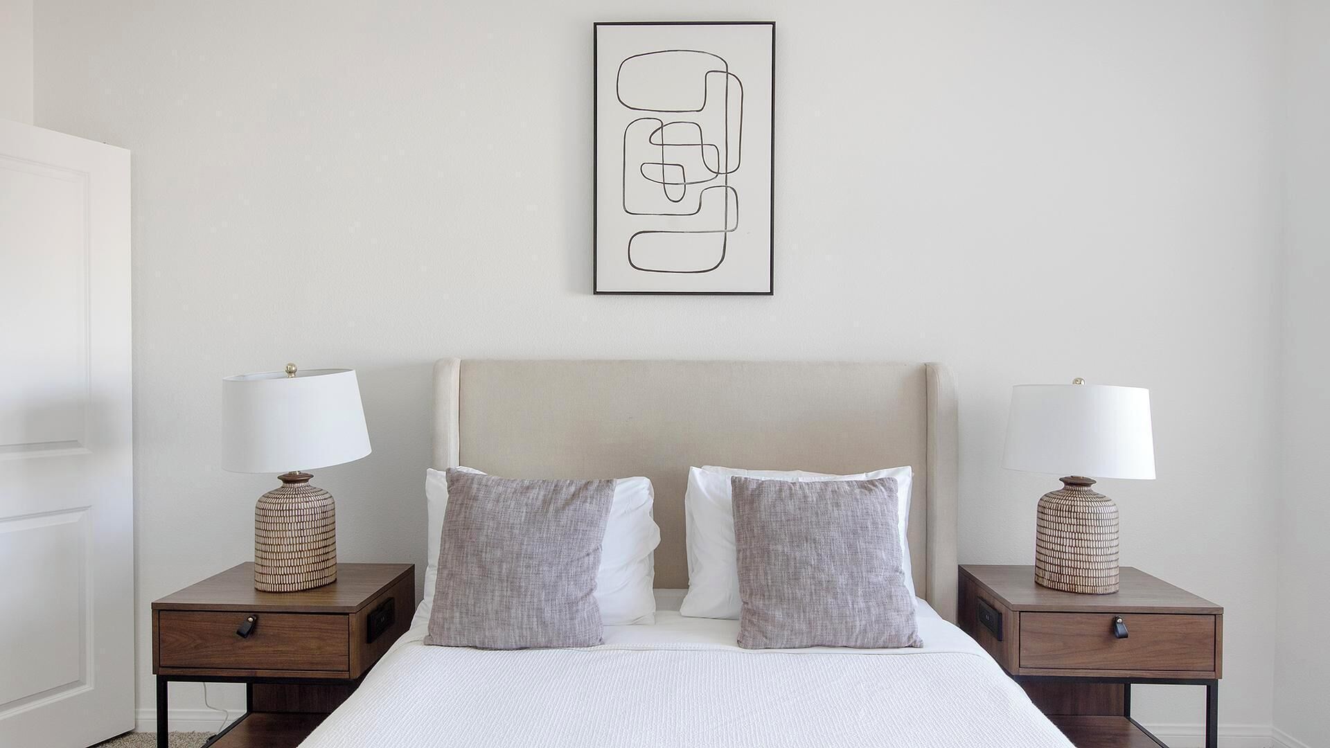Una camera da letto con un letto, due comodini con lampade e un'opera d'arte astratta incorniciata al muro.