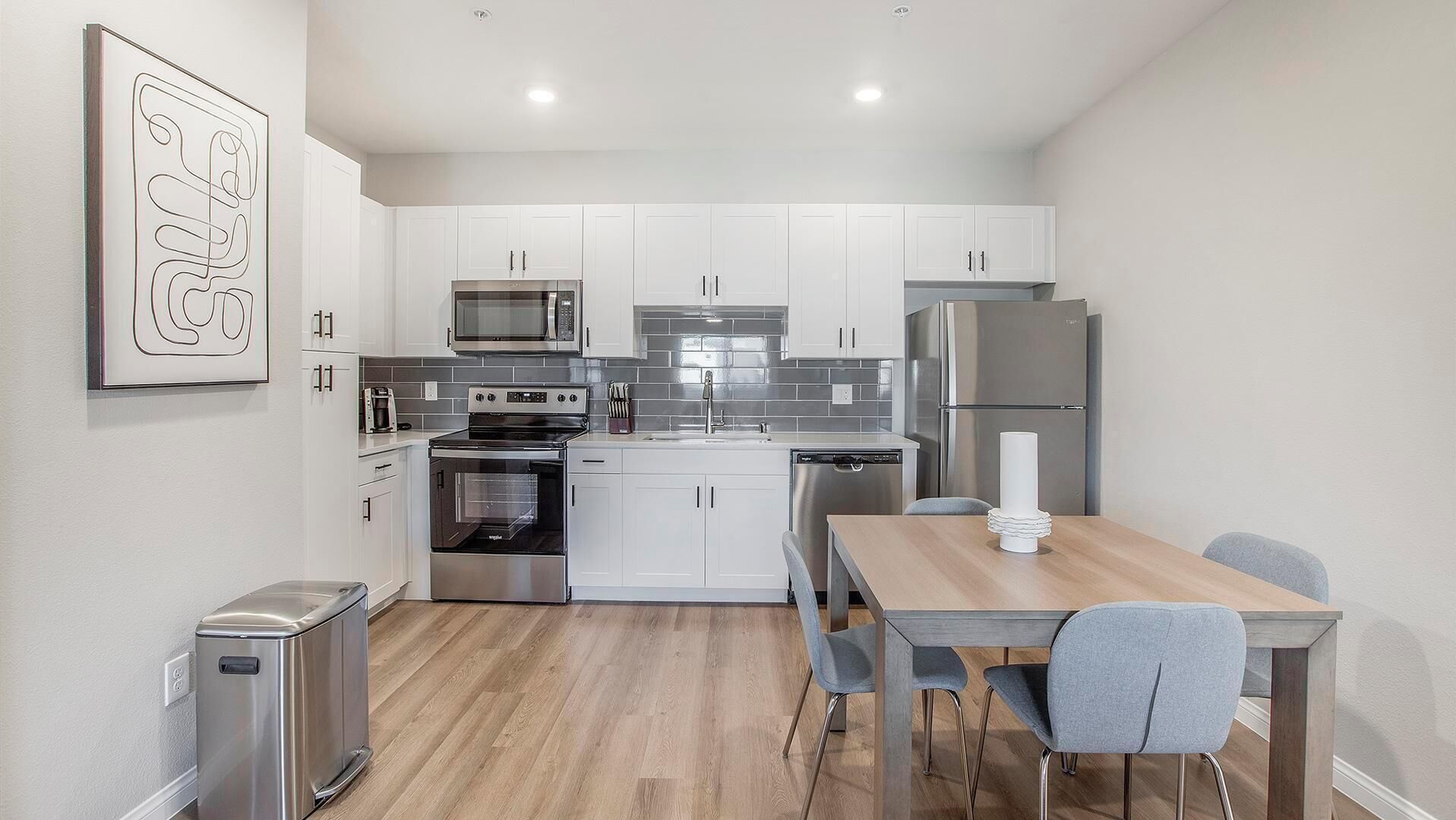 A modern kitchen with white cabinets, stainless steel appliances, and a wooden dining table with two chairs.