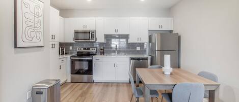 A modern kitchen with white cabinets, stainless steel appliances, and a wooden dining table with two chairs.