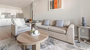 Un salon moderne avec un canapé gris, une table basse ronde et une cuisine en arrière-plan.