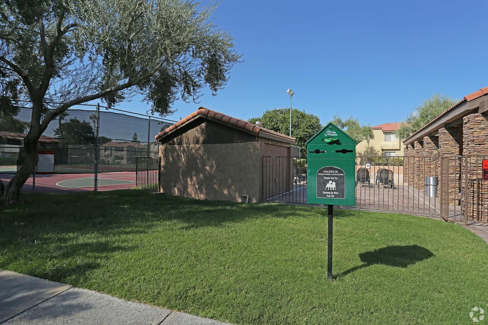 Ein grüner Briefkasten mit Recycling-Symbol, ein durch Zäune umgrenzter Basketballplatz und ein Steinhaus mit rotem Dach.