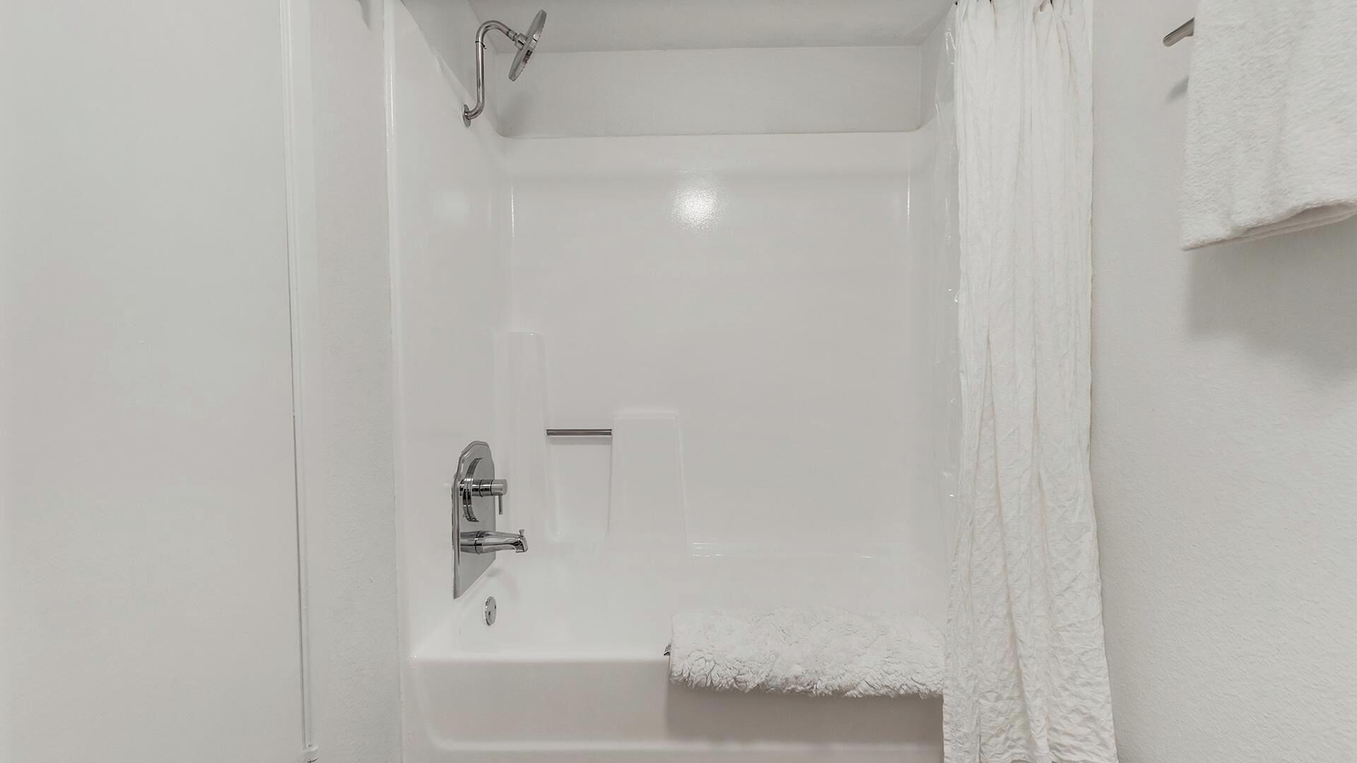 A white bathtub with a showerhead and faucet, a small window, and a towel hanging on the wall.