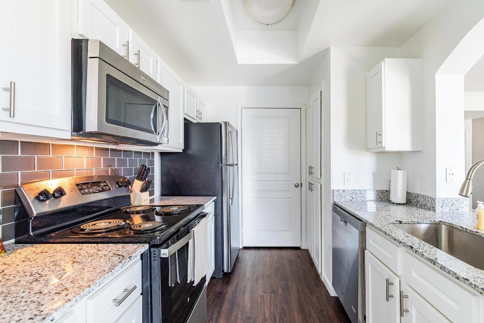 A modern kitchen with white cabinetry, stainless steel appliances, and a granite countertop.