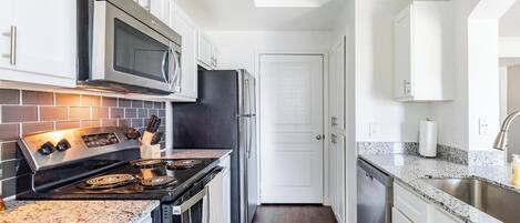 A modern kitchen with white cabinetry, stainless steel appliances, and a granite countertop.