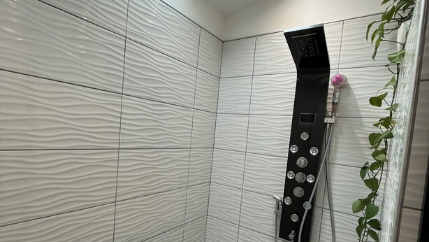 Un área de ducha moderna con un banco integrado, un cabezal de ducha manual y una planta en la pared.