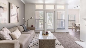 Ein geräumiges Wohnzimmer mit einem beigefarbenen Sofa, einem Couchtisch und einem großen Fenster mit Jalousien.