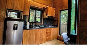 Une cuisine compacte avec des meubles en bois, un réfrigérateur en acier inoxydable et une fenêtre donnant sur un espace verdoyant.