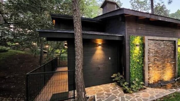 Une maison moderne avec un chemin de pierre menant à une terrasse en bois, le tout entouré de verdure.