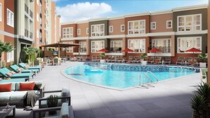 Un espace piscine d’hôtel avec des chaises longues et des parasols, entouré d’immeubles à plusieurs étages dotés de balcons.