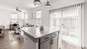 A modern kitchen with a granite countertop, a built-in oven, and a large window with blinds. - Landing | Stunning 1BD, Pool, Yoga Studio (Fort Worth)