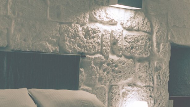 A bed with pillows and a rolled towel, a nightstand, and a wall with a stone texture. - Charming 3-bedroom bed & breakfast in peaceful Capurso with AC (Capurso)