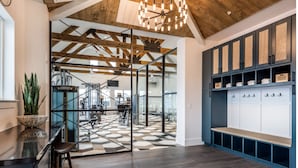 A spacious room with a high ceiling, exposed wooden beams, and a large open area with exercise equipment. There is a seating area with a bench and a potted plant. - Landing | Stylish 1BD, Clubhouse, Gym (Fort Worth)