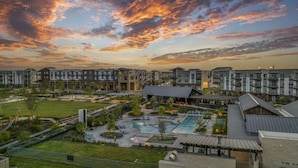 A modern apartment complex with multiple buildings, a central courtyard with a swimming pool, and a scenic sunset view.