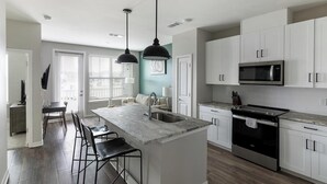 Une cuisine moderne avec des meubles blancs, un îlot central doté de tabourets, un four à micro-ondes encastré et une cuisinière.