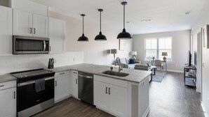 Una cocina moderna con armarios blancos, microondas integrado, estufa y lavavajillas. Hay tres lámparas colgantes sobre la isla.