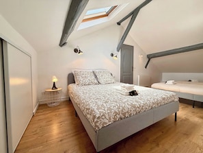 A bedroom with a skylight, a bed with a patterned bedspread, a bedside table with a lamp, and a small side table. - 10' Disneyland & Parking - 9 personnes (Ferrières-en-Brie)