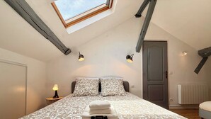 Un dormitorio con tragaluz, cama con ropa de cama estampada, lámparas de noche, una puerta y un radiador.