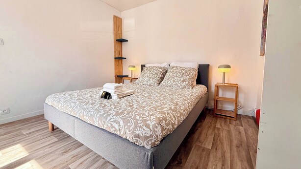 A neatly made bed with a patterned bedspread, two bedside lamps, and a wooden shelf unit.