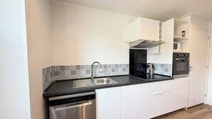 Una cocina moderna con armarios blancos, lavavajillas de acero inoxidable, estufa negra y azulejos decorativos en la pared.