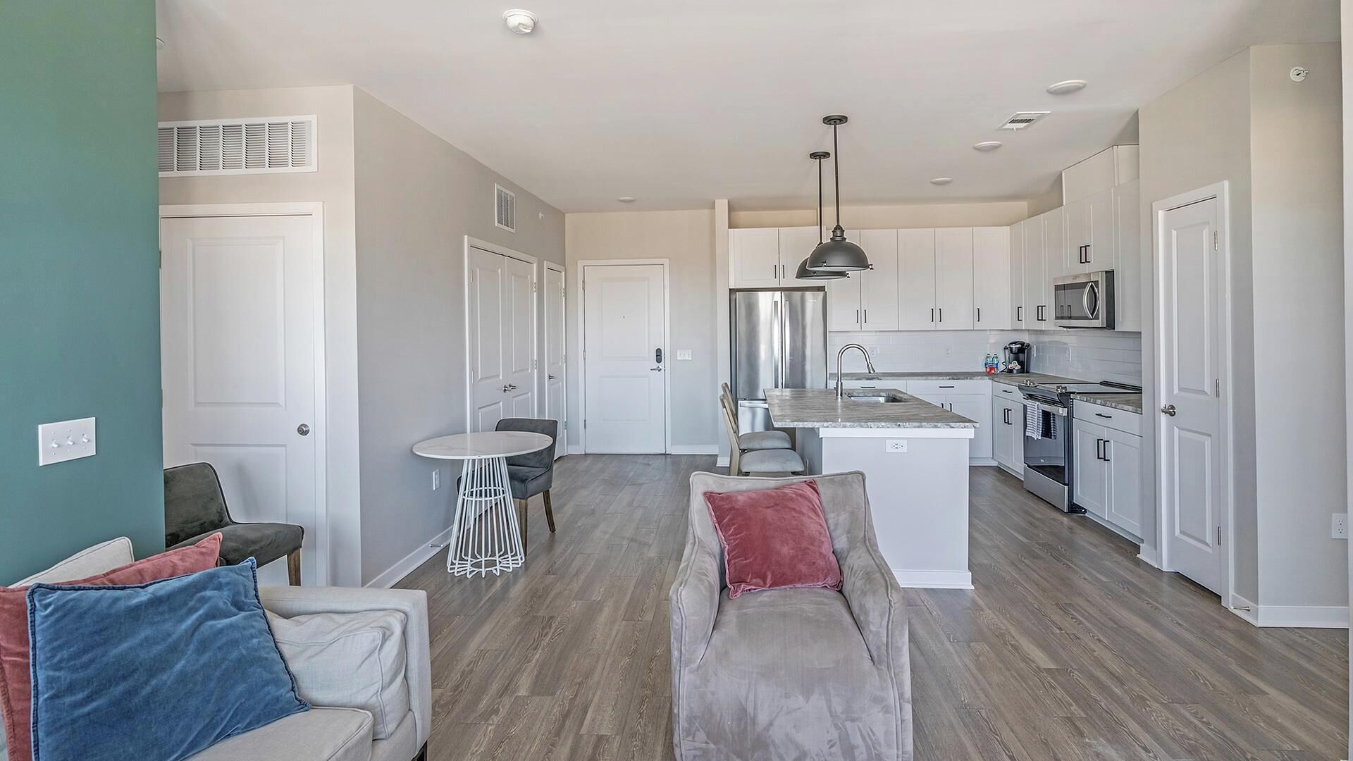 A modern kitchen with white cabinets, a stainless steel refrigerator, and a microwave. There is a dining area with a round table and two chairs.