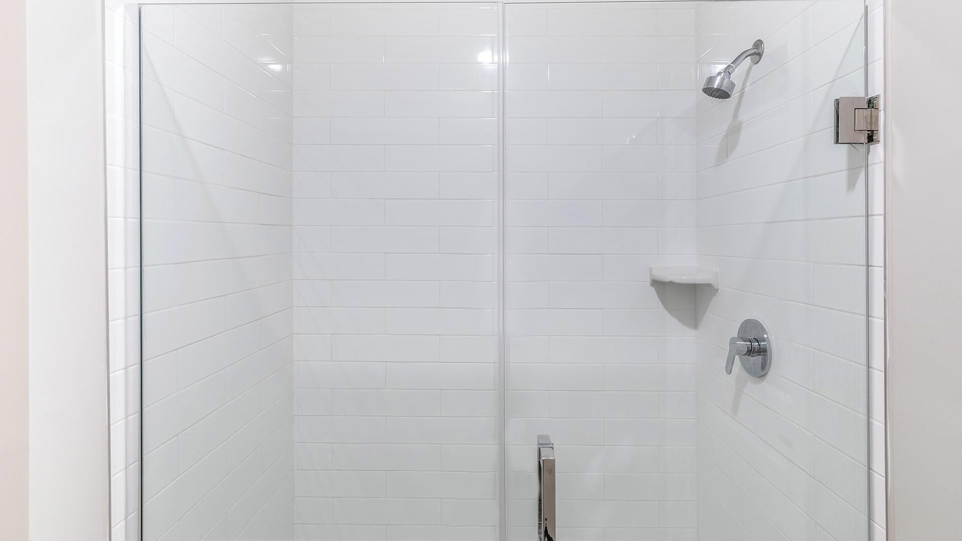 A glass-enclosed shower with white tiles, a handheld showerhead, and a wall-mounted faucet.