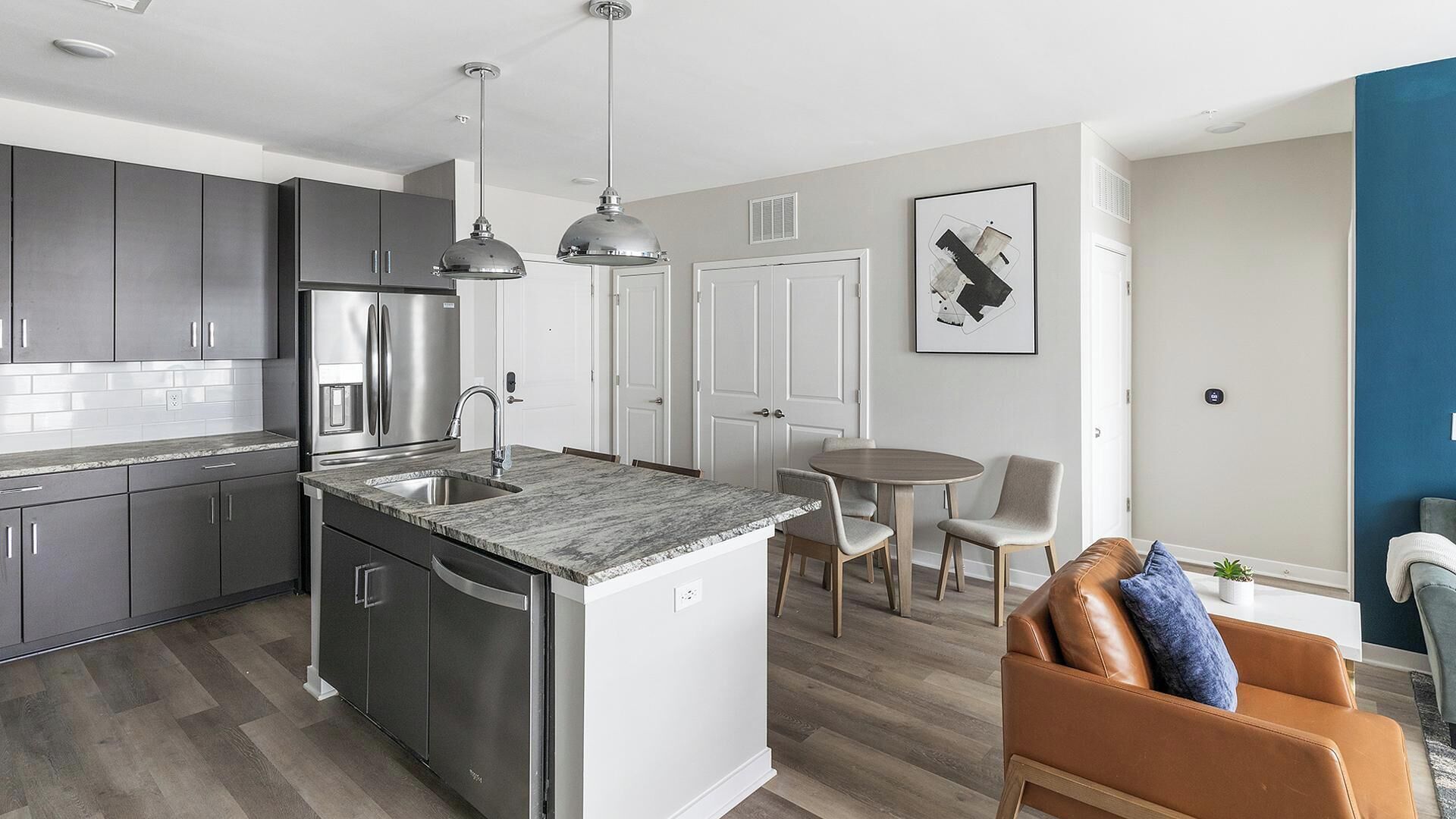 A modern kitchen with stainless steel appliances, a marble countertop, and a dining area with a round table and chairs.