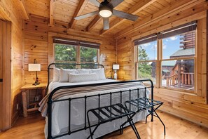 A wooden cabin bedroom with a bed, two bedside lamps, a ceiling fan, and large windows. - OMG VIEWS! Gameroom~Hot tub~Outdoor Pool~ Suana (Sevierville)