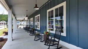A covered porch with rocking chairs and potted plants, overlooking a street. - Landing | Spectacular 1BD, Gym, Clubhouse (Huntsville)