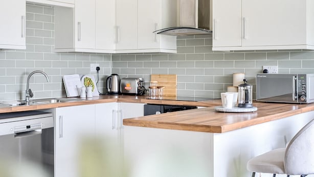 A modern kitchen with white cabinets, a wooden countertop, a built-in oven, and a microwave. - Beautiful apartment in Claygate Village (Claygate)