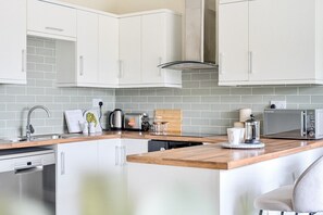 Uma cozinha moderna com armários brancos, bancada de madeira, forno embutido e micro-ondas.