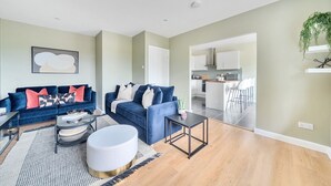 A modern living room with a blue sofa set, a round white ottoman, and a coffee table. - Beautiful apartment in Claygate Village (Claygate)