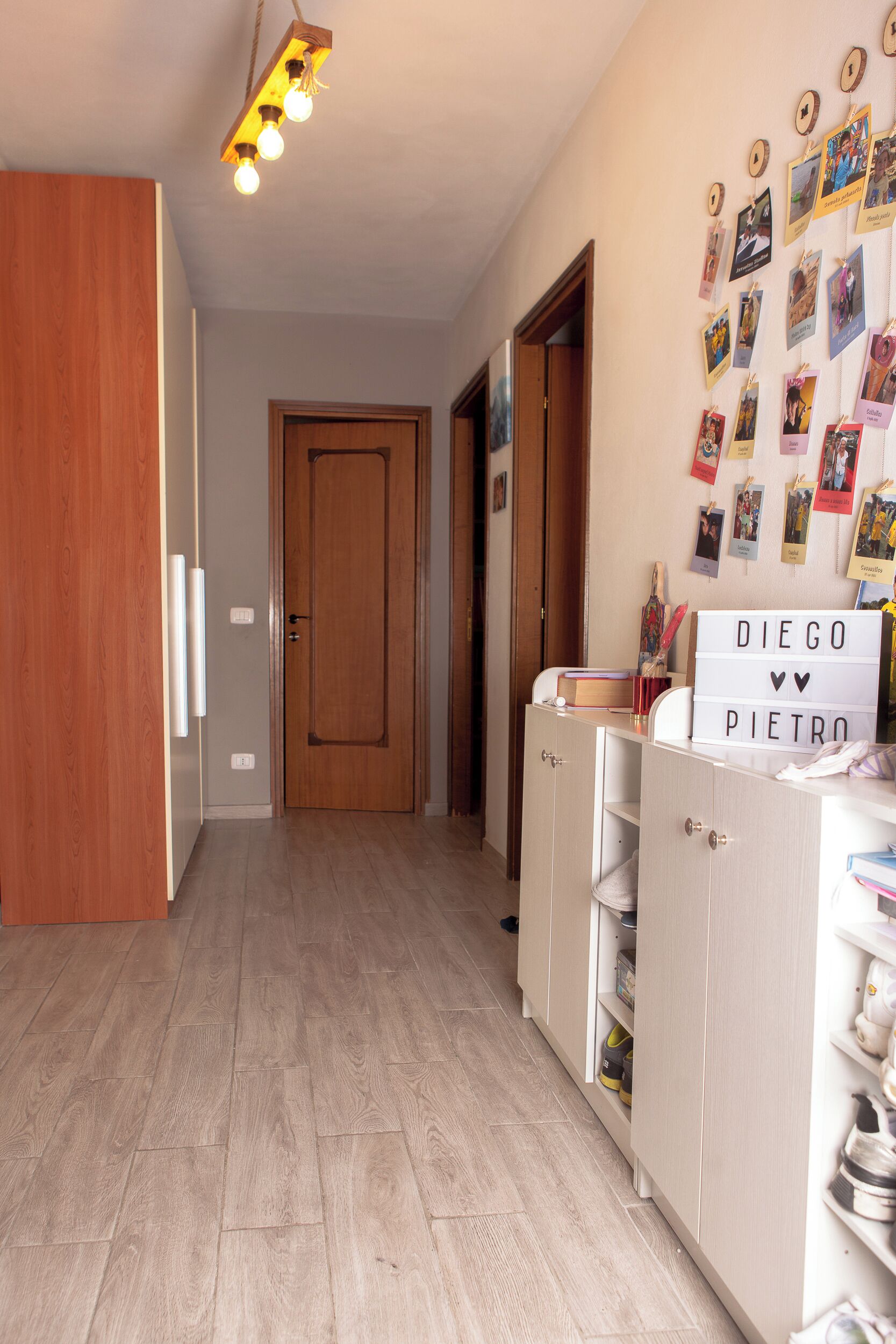 A hallway with wooden flooring, a door at the end, and a wall with personal photos and a sign that reads 'DIEGO PIETRO'.