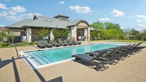 A swimming pool with lounge chairs, a covered area, and a brick building with a sloped roof. - Landing | Beautiful 1BD, Pool, Gym (Dallas)