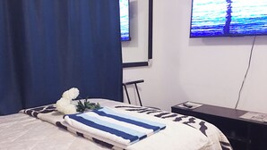 A neatly made bed with a striped blanket, a white flower, and a blue curtain.