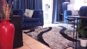 A living room with a blue sofa, a red vase, and a black lamp.