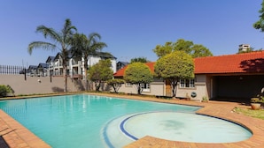 A swimming pool with a curved section, surrounded by a brick patio.