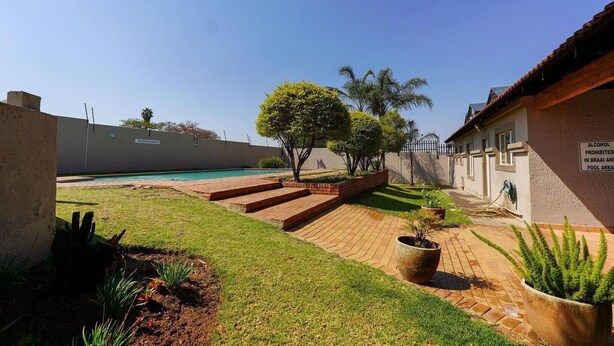 A pool area with a brick pathway, a small tree, and a sign prohibiting alcohol.