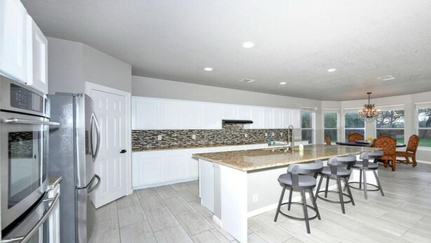 Una cocina moderna con armarios blancos, encimera de granito y una isla central con taburetes de bar.