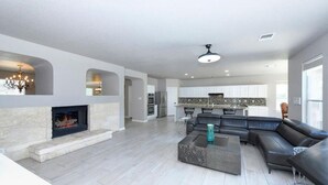 Un amplio salón con chimenea, un sofá modular y una cocina moderna al fondo.