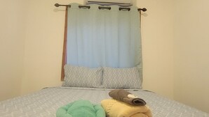 Une chambre à coucher avec un lit, une fenêtre avec un rideau et un appareil de climatisation fixé au mur.