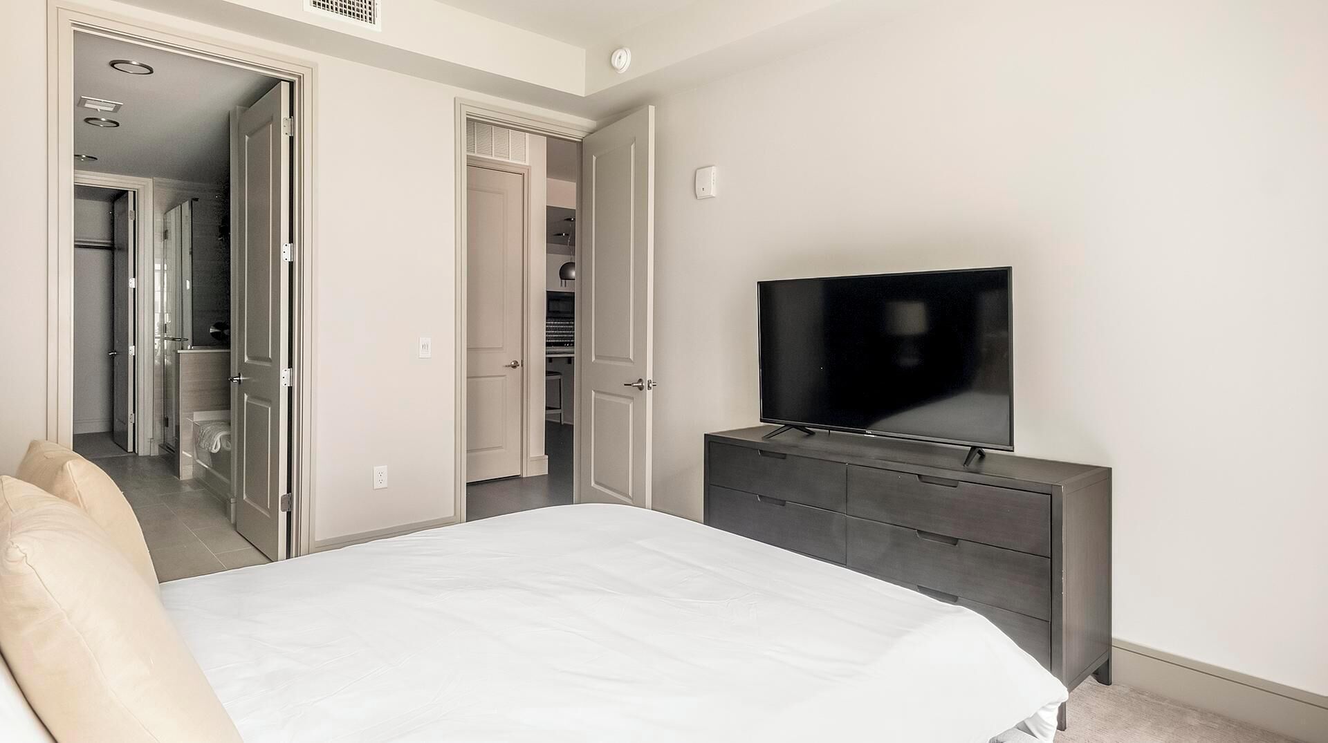 A bedroom with a bed, a TV on a dresser, and a walk-in closet.