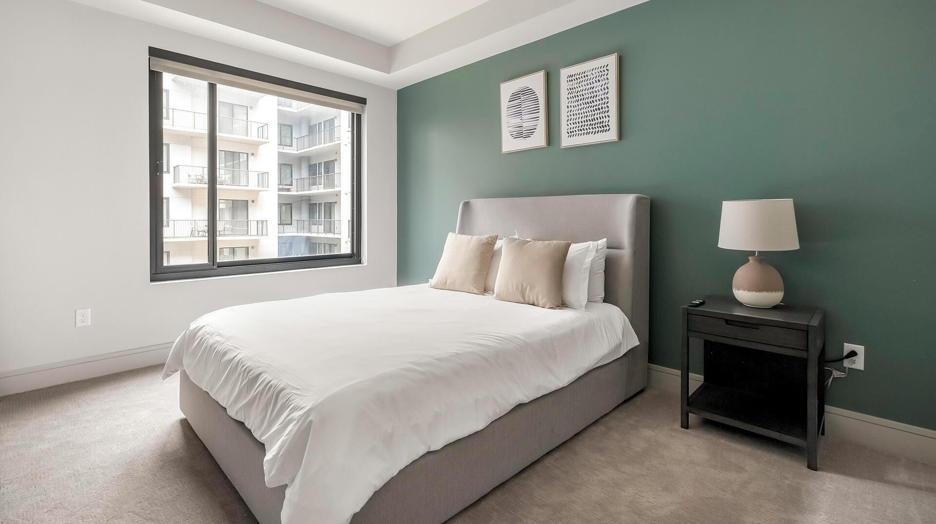 A bedroom with a large bed, a nightstand, a lamp, and artwork on the wall.