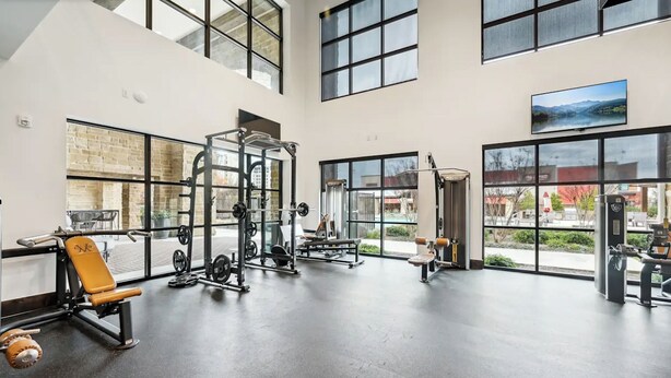 A spacious gym with various exercise equipment, large windows, and a view of the outdoors.