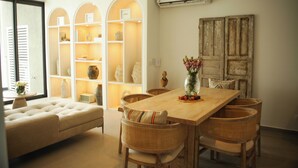 A dining area with a wooden table, wicker chairs, and a sofa. There are shelves with decorative items and an air conditioning unit on the wall. - Stylish Oceanfront Condo w/ Jacuzzi, Pool & Gym (Bucerías)