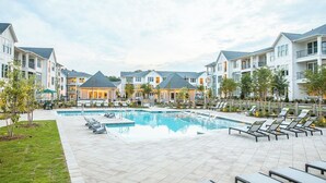 A pool area with lounge chairs and a building with multiple balconies.