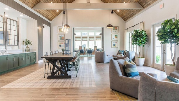 A spacious room with a wooden ceiling, a dining table with chairs, a sofa, and potted plants.