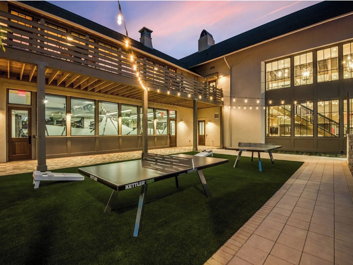 An outdoor area with ping pong tables, a covered seating area, and a building with large windows.