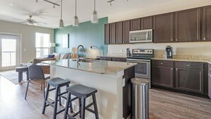 A modern kitchen with dark wood cabinets, a large island with bar stools, stainless steel appliances, and a teal accent wall.
