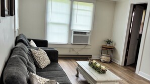 Ein Wohnzimmer mit einem dunkelgrauen Sofa, einem weißen Couchtisch und einem kleinen Beistelltisch mit einer Pflanze.