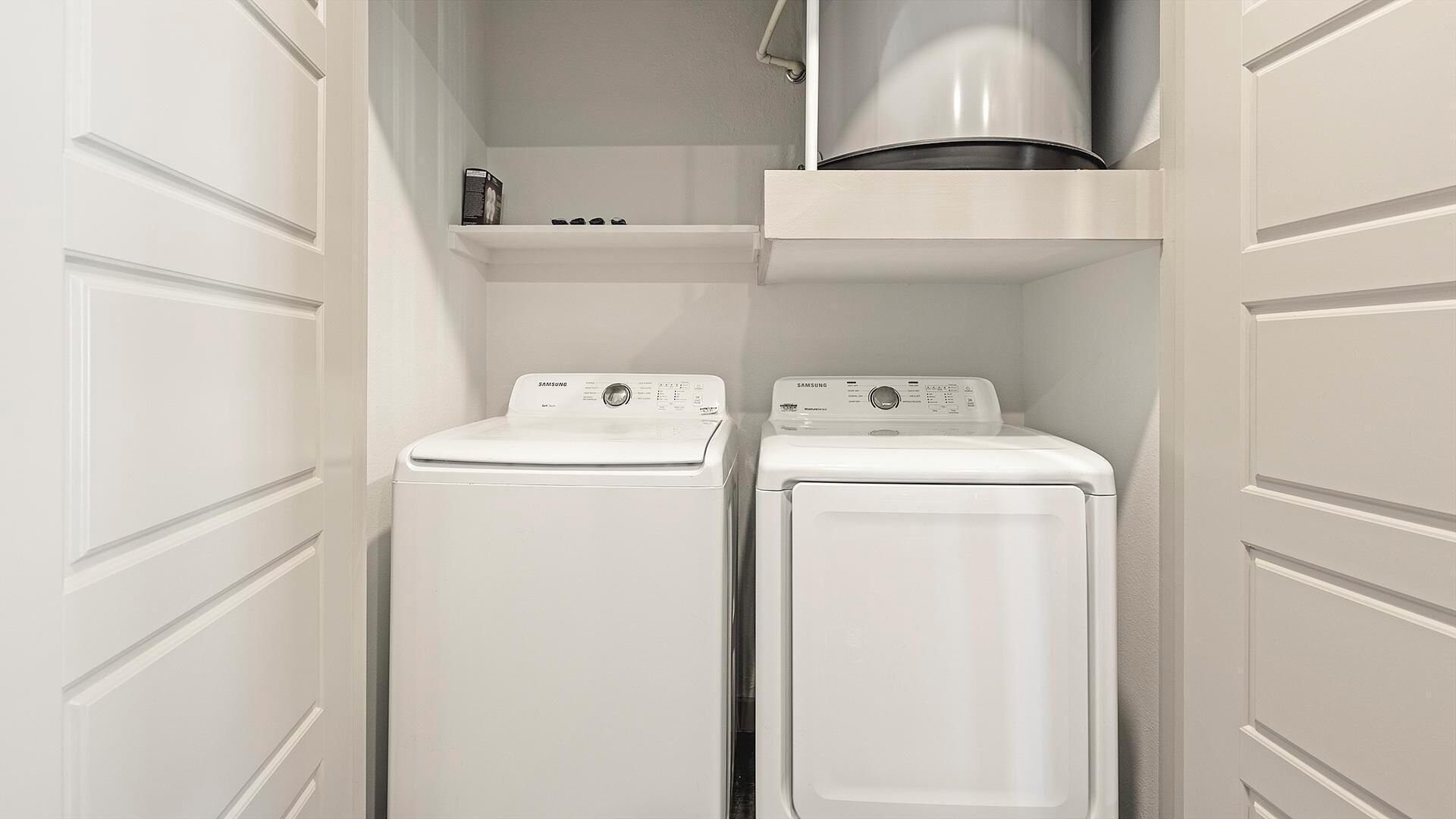 A laundry room with two white front-loading washing machines and a stainless steel dryer.